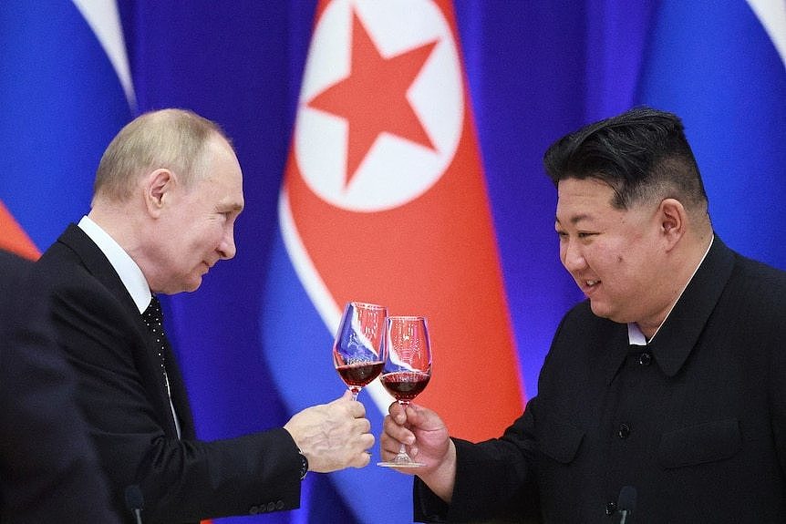 Two men in suits smiling, while holding glasses of wine and looking at each other