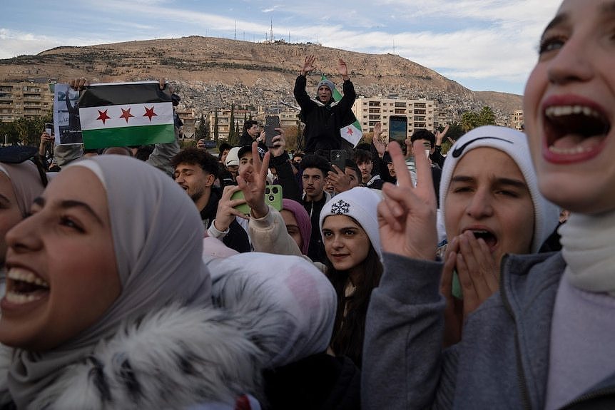 People gather in a large group shouting in celebrating and holding their fingers up in a 'v' shape