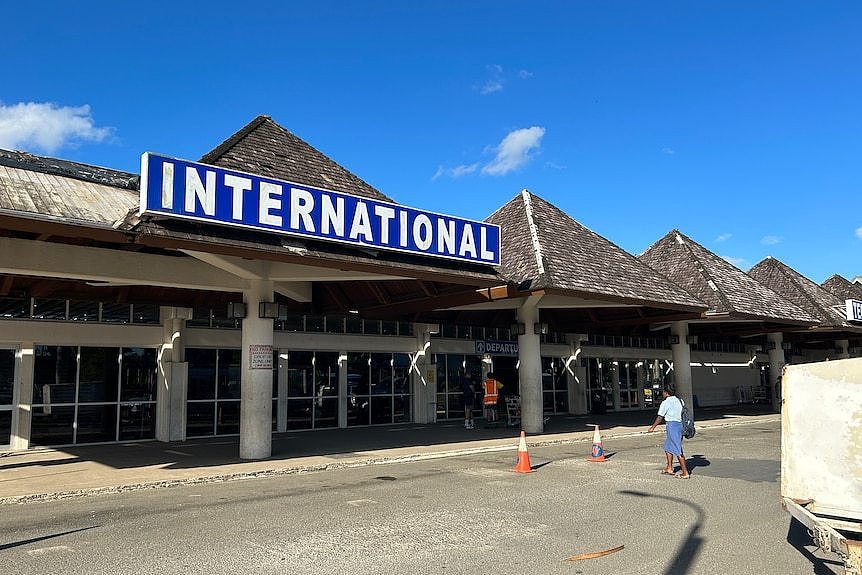 A woman walks towards an airport entry with a sign saying 'international'.