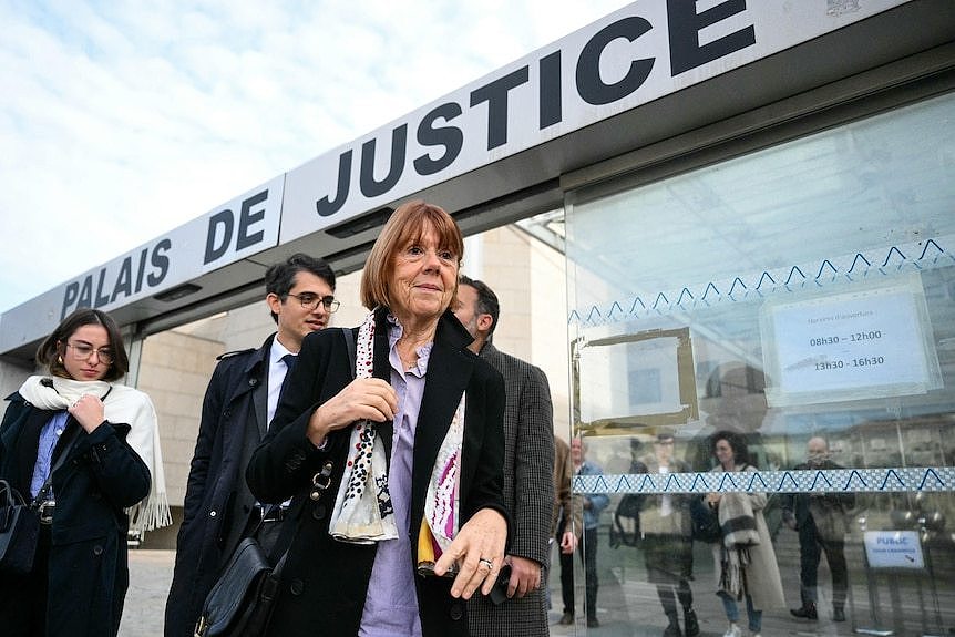 An older woman in a red-blonde bob wearing a patterned scarf walks out of a building with 'Palais de Justice' on it'