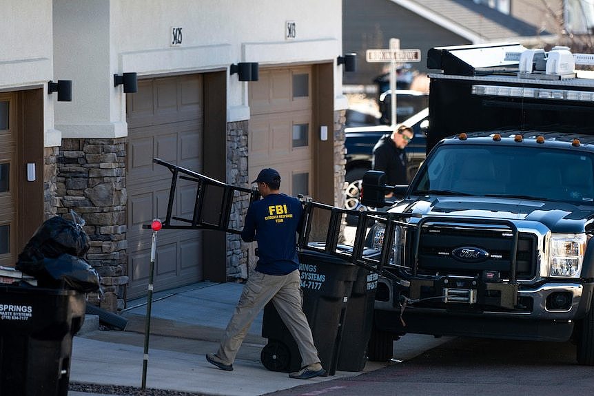 A man in an FBI jacket carries a ladder into a building