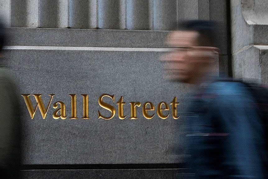 person who is blurred walks in front of the new york stock exchange, sign says wall street