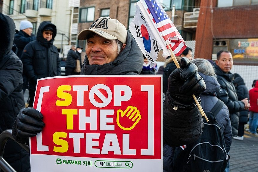 man wearing black puffer jacket holds protest sign red