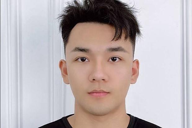 A Chinese man wearing a black muscle tee staring emotionless at the camera on a white door backdrop