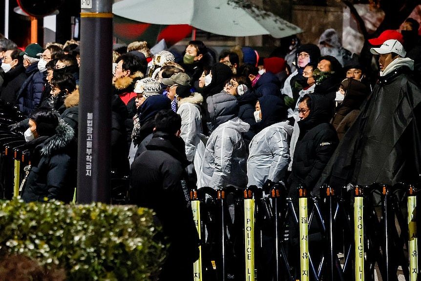 People wearing face masks and winter jackets stand outside South Korean president's residence in support