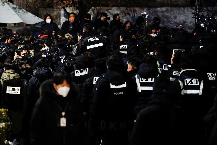 Dozens of police officers wearing vests gather outside the residence of South Korean President Yoon Suk Yeol