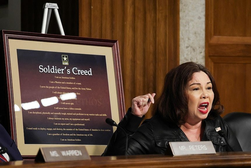 A woman yelling in front of a soldiers creed sign. 