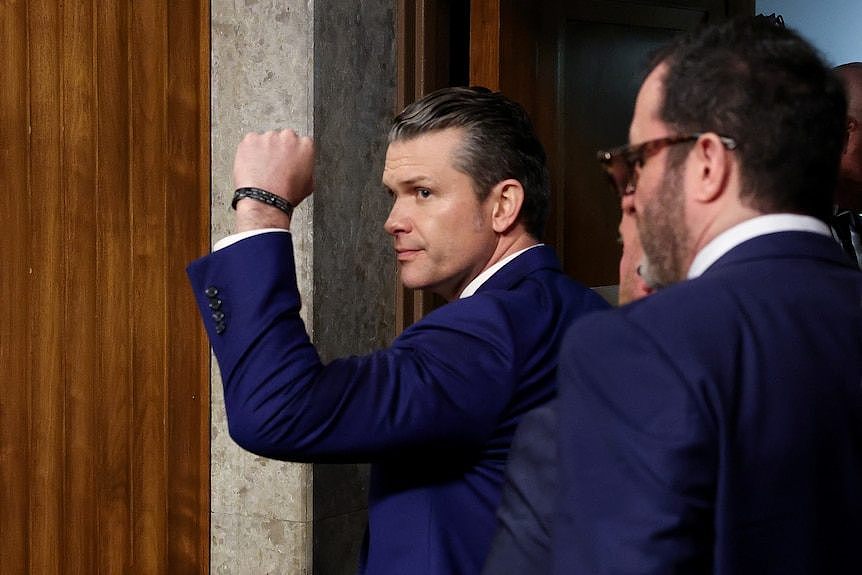 Pete Hegseth shaking a fist walking out a door. 