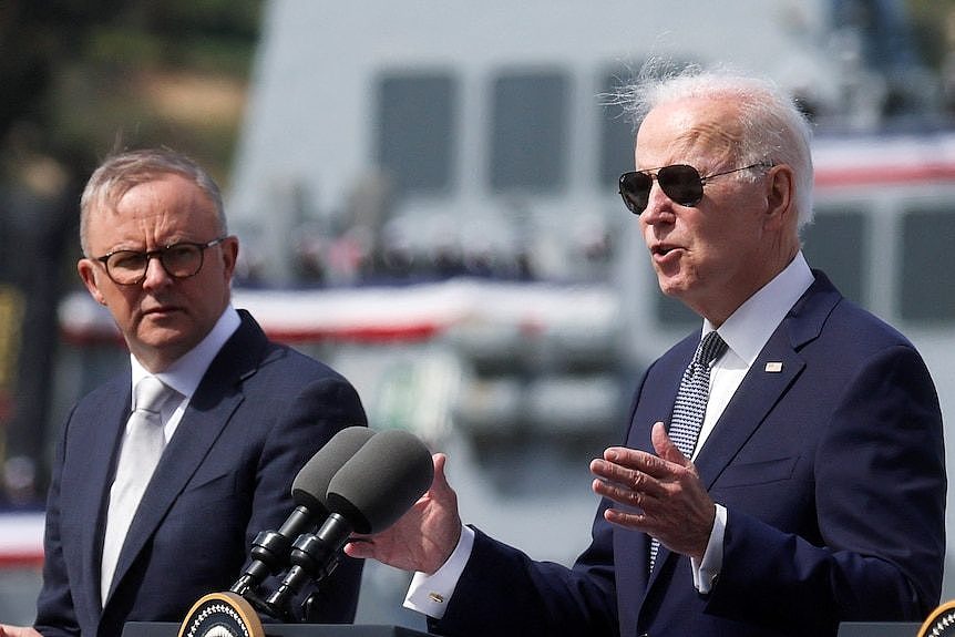 One man smiles and another maintains a neutral expression as they look in front of where they stand