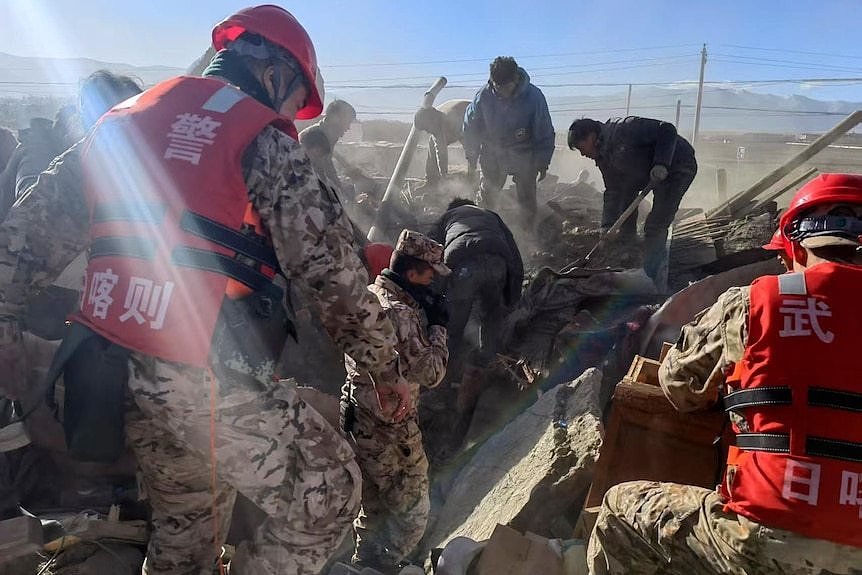 Rescue crews in military fatigues search rubble with locals looking for survivors of a powerful earthquake.