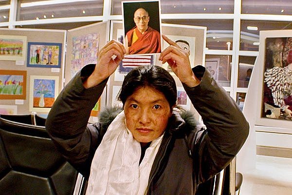 Ngawang Sangdrol is seated while holding a portait photo of smiling Dalai Lama over her head.