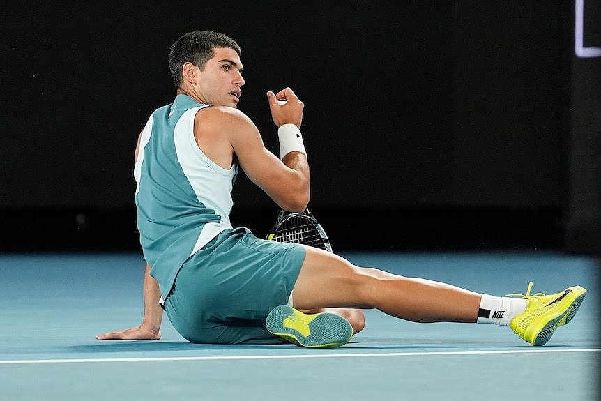 Carlos Alcaraz lays on the floor holding his racquet