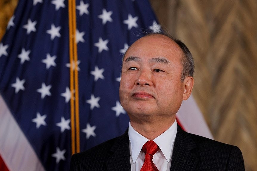 a japanese older man in a suit stands in front of a US flag