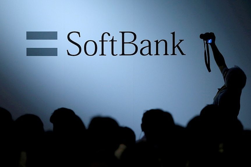 a crowd stands in front of the softbank logo on a wall 