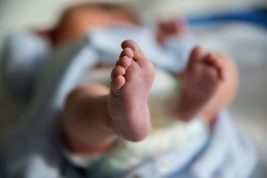 A newborn baby is shown lying down, with one of its feet in the foreground of the image.