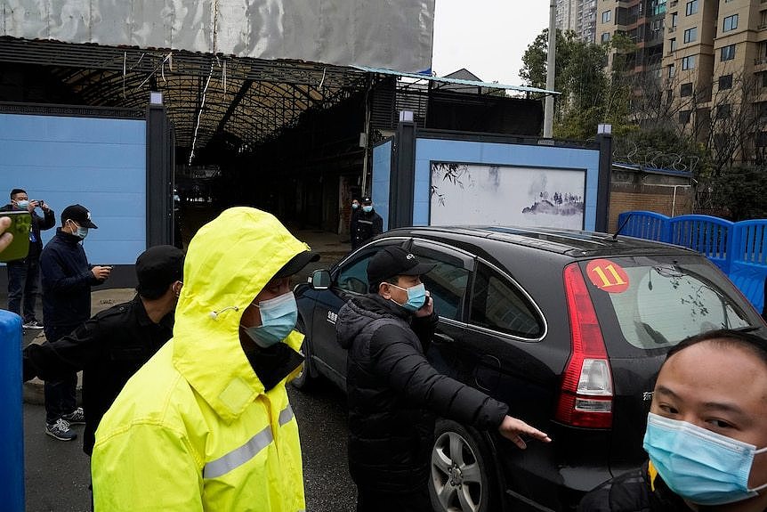 Asian people in masks stand around as a car enters a large structure