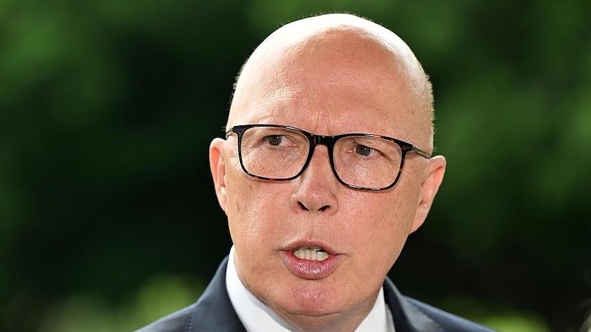 A middle-aged bald man with glasses in a suit speaks outside.