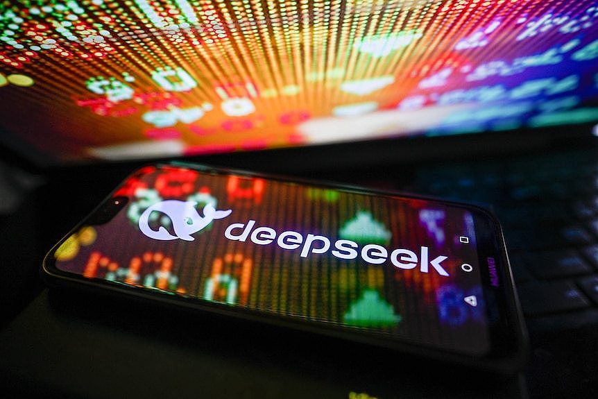 A white DeepSeek logo on a smart phone is illuminated by colourful stock market percentages.