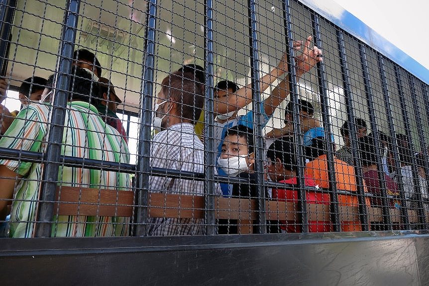 People behind the bars of a vehicle transporting them between detention centres