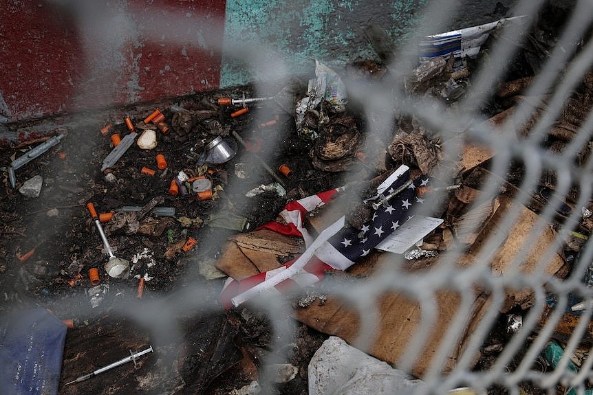 Used needles left by drug users lies next to a tattered US flag