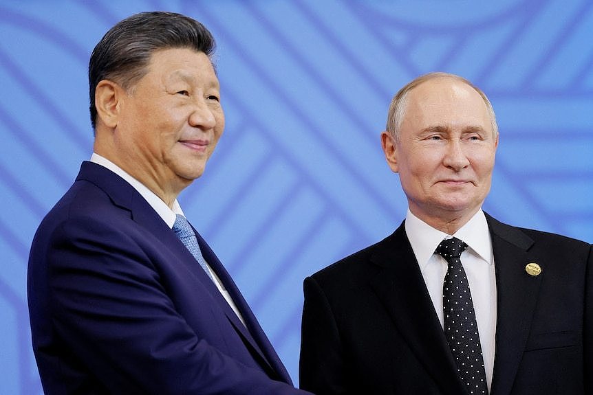 Xi Jinping wearing a navy suit jacket and smiling next to a smiling Vladimir Putin in a black suit