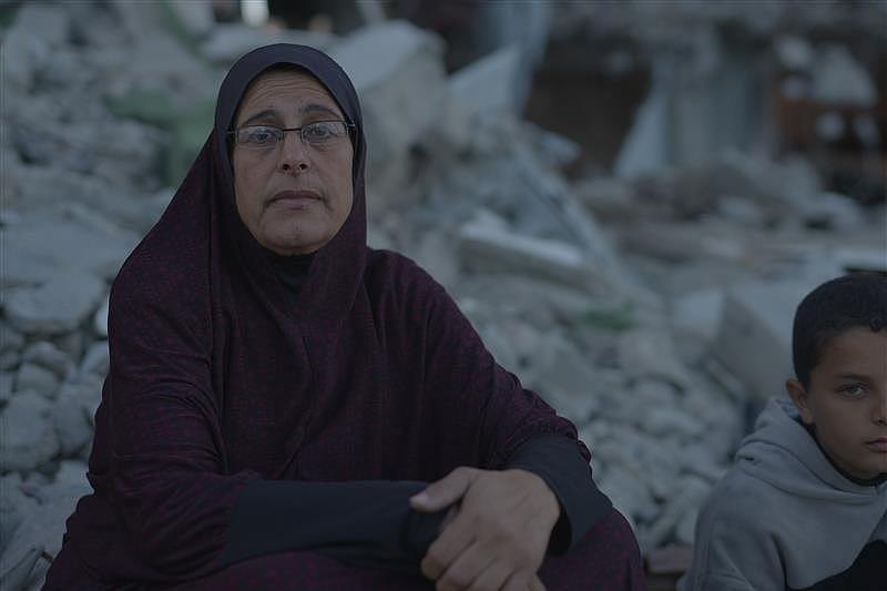 A woman wearing traditional Islamic dress, sitting in a pile of rubble.