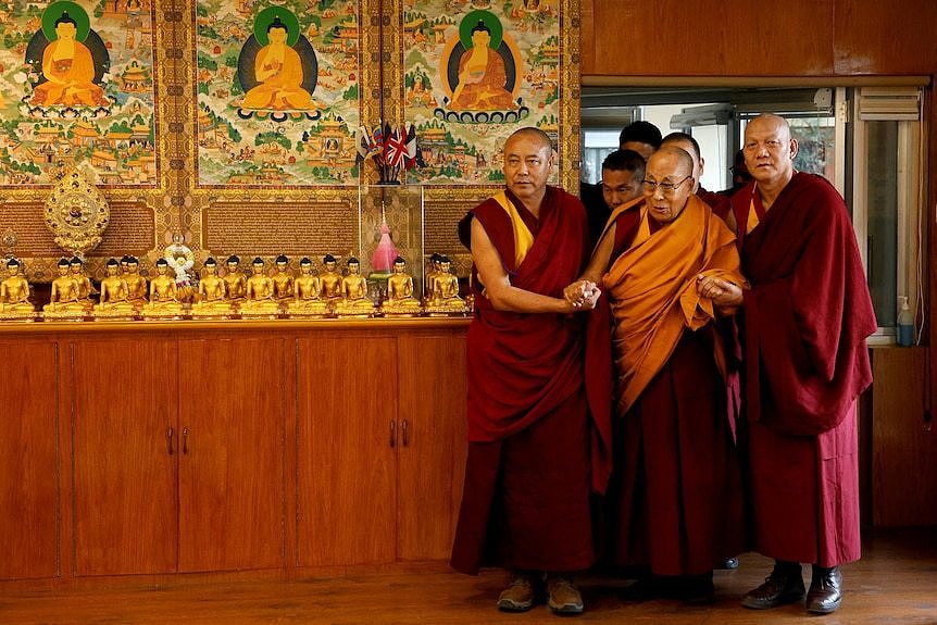 Tibetan spiritual leader, the Dalai Lama, is escorted into a hall by monks holding his hands