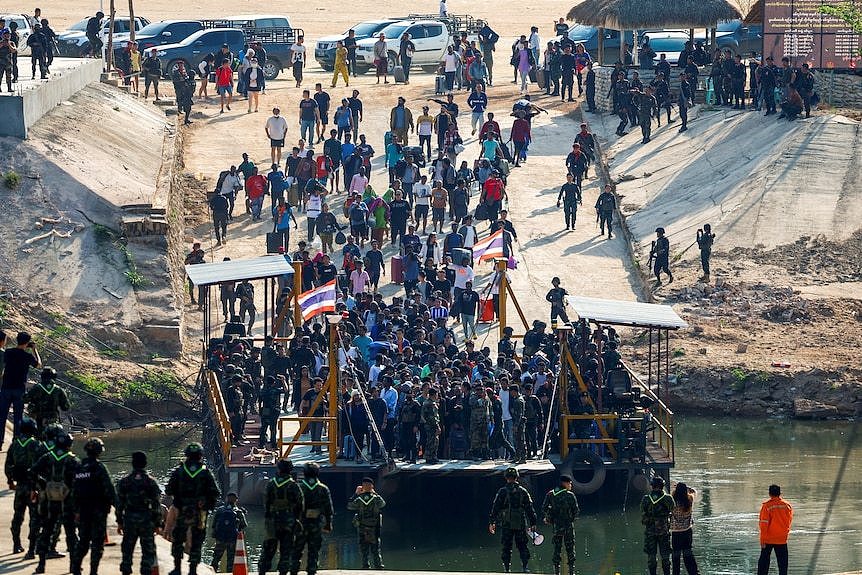 Multinational victims of scam centers walk towards a vessel in order to cross Moei River to Thailand.