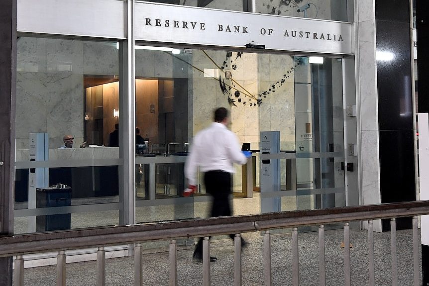 A person in a long sleeved white collared shirt and black pants walks into the Reserve Bank of Australia as its doors slide open