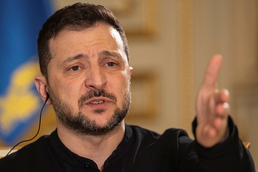 Volodymyr Zelenskyy at a press conference with the Ukrainian flag in the background.