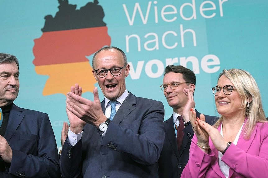 A group of people clapping behind a poster with the German flag.