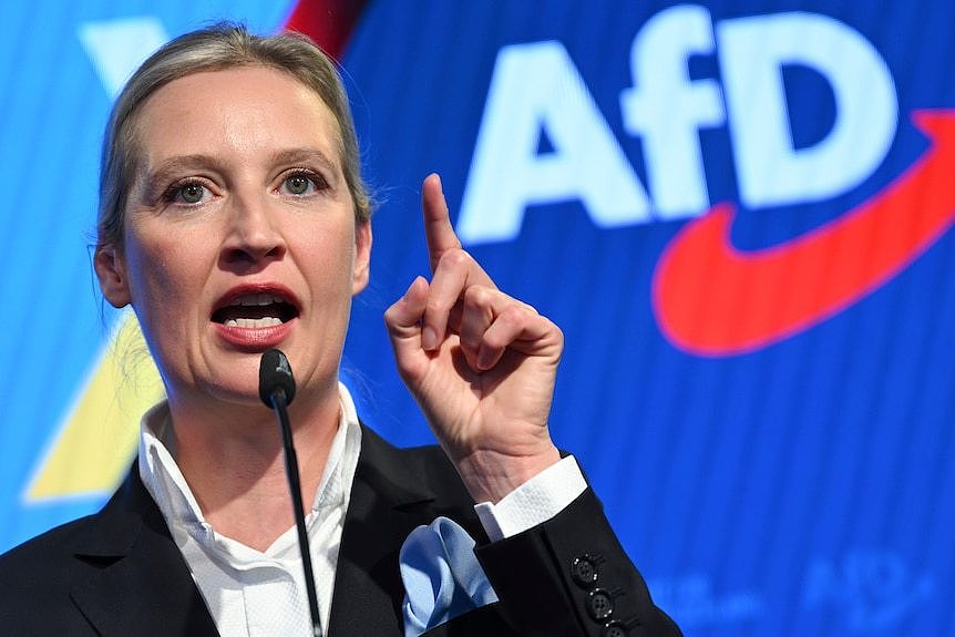 A woman standing behind a microphone pointing with one finger up.