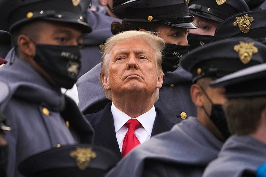 Former president Donald Trump is surrounded by army cadets while watching a football game.