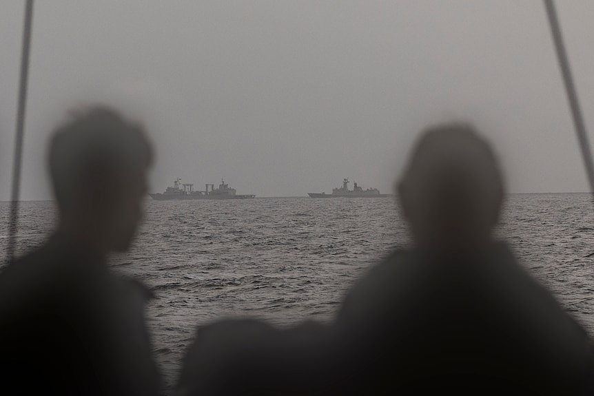 Chinese vessels on the horizon are watched by silhouetted sailors.