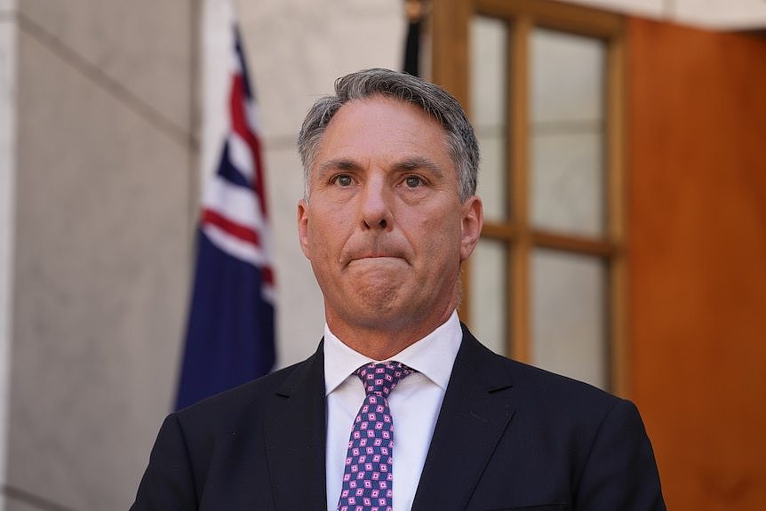 Man listening to reporters' question, Australian flag behind him