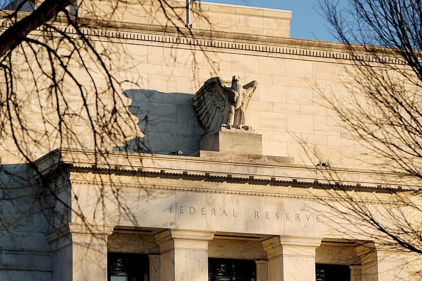 The concrete stone exterior of the US Federal Reserve Building framed by tree branches along with a statue of an eagle