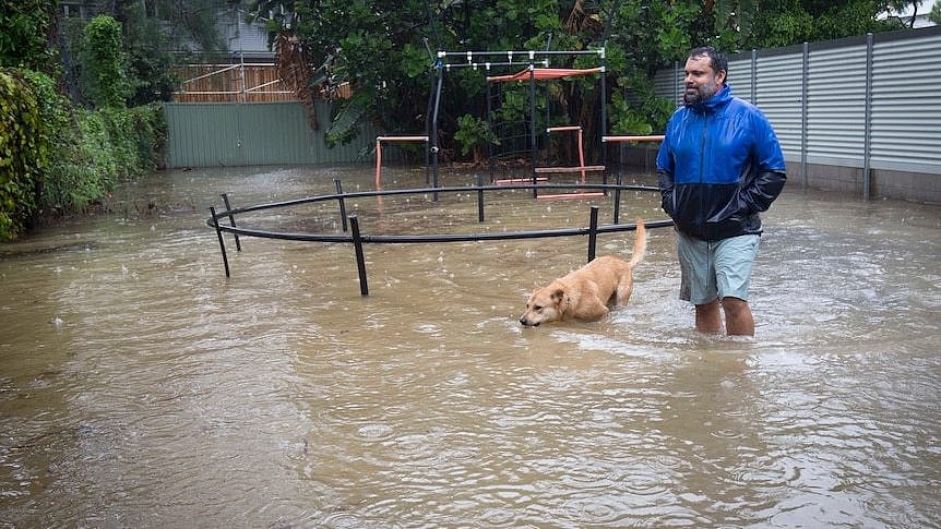 Man with floodwaters up to his shins stands with dog in backyard