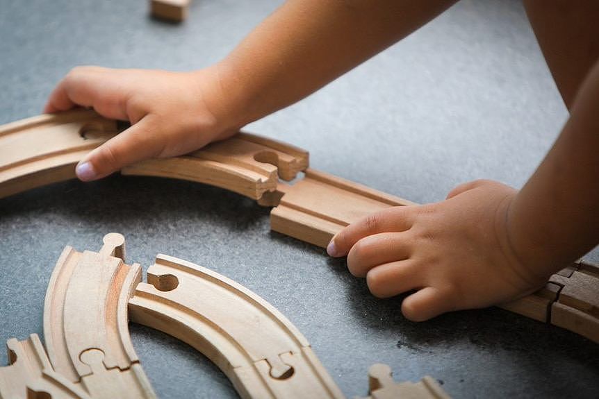 A child playing with wooden train tracks.