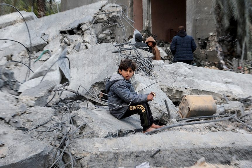 A young boy sits on rubble of a collapsed concrete building after an air strike.