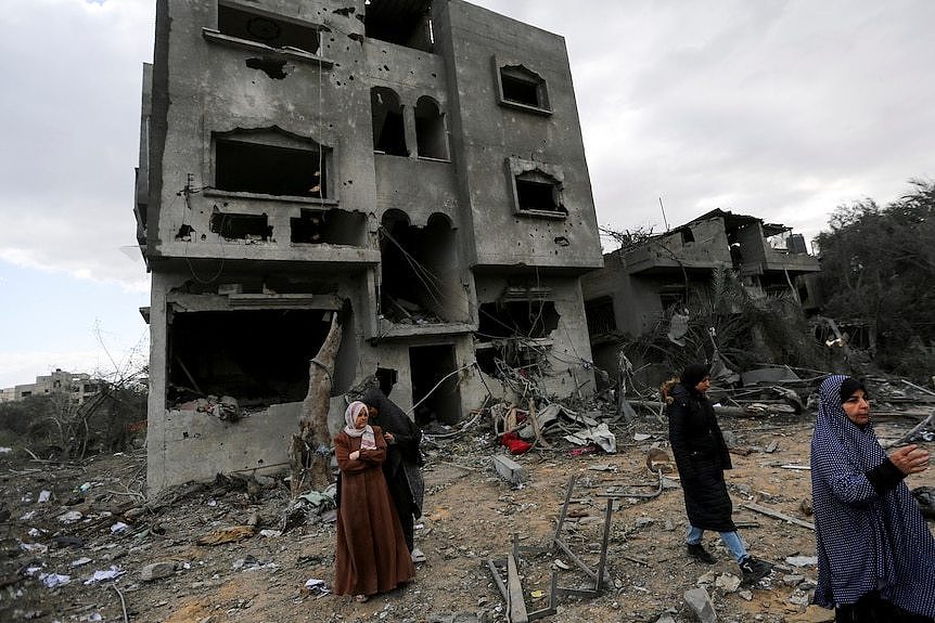 A group of women walking around the base of a severely damaged three-storey house in Gaza.